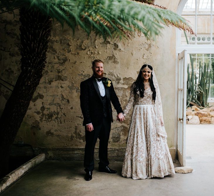 Bride in ivory and gold embellished wedding dress and groom in tuxedo at Syon Park conservatory reception