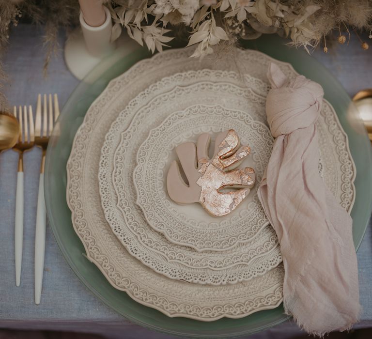 Place setting with vintage plates. white cutlery, blush linen and biscuit favour 