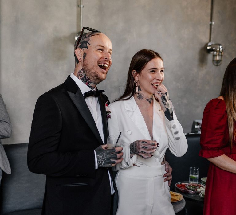 Tattooed bride and groom laughing during the wedding speeches 