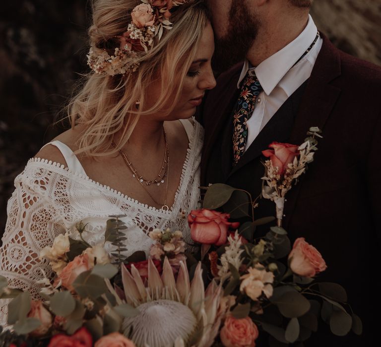 Dusky pink flower crown worn by bride in a boho lace tassel wedding dress with layered gold necklaces and a large autumnal bouquet of roses