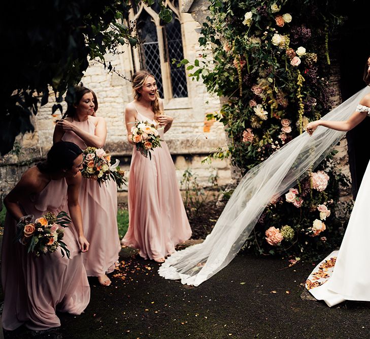 Bride celebrating with her bridesmaids with long flowing veil and peach bridesmaids dresses