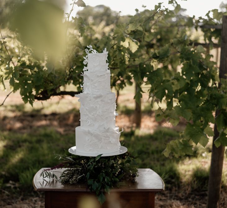 White iced wedding cake with intricate detail on a dresser in a vineyard 