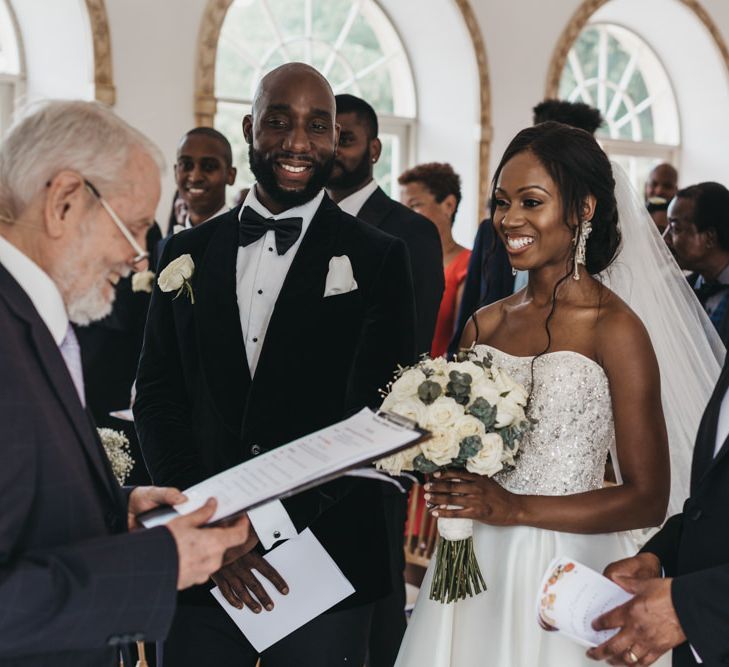 Black bride in a strapless Oleg Cassini wedding dress being given away at the altar by her father 