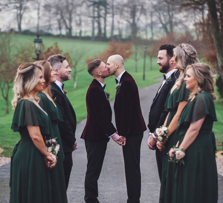 two grooms kissing at the end of the wedding party line 