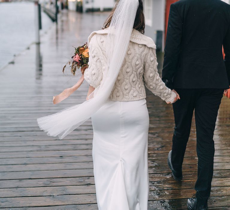 The bride and groom walk hand in hand along the boardwalk in Sweden