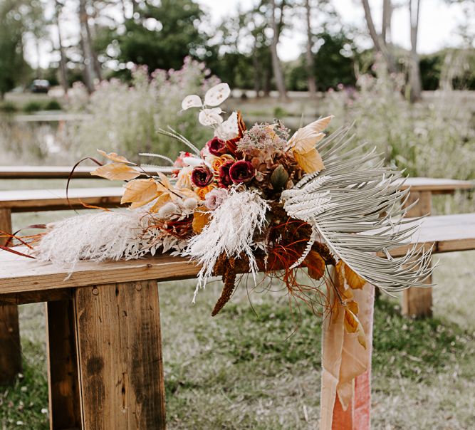 Dried floral bouquet tied with ribbon sits upon wooden bench outdoors