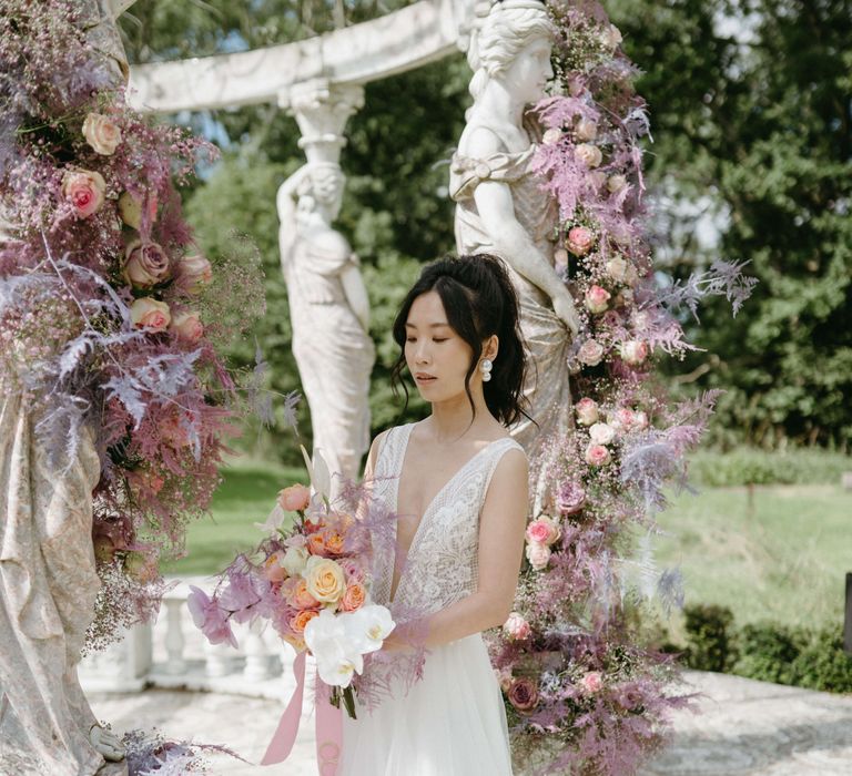 Dark haired Asian bride stands surrounded by lilac flowers 