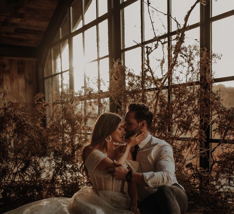 Bride in an off the shoulder wedding dress with sparkly design sitting on the floor at Hidden River Cabins with dried flower decor 