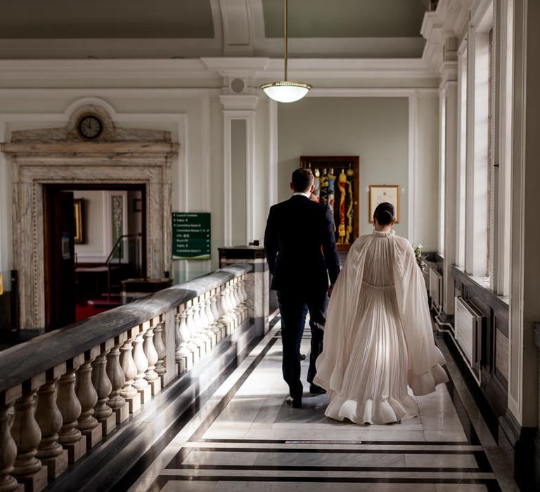 Bride in a long sleeve bridal cape with ruffle hem walking through the halls at Islington Town Hall