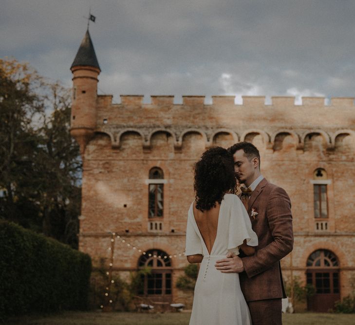 Bride and groom portrait in front of Château de Caumont with bride in a low V back wedding dress with button detail 