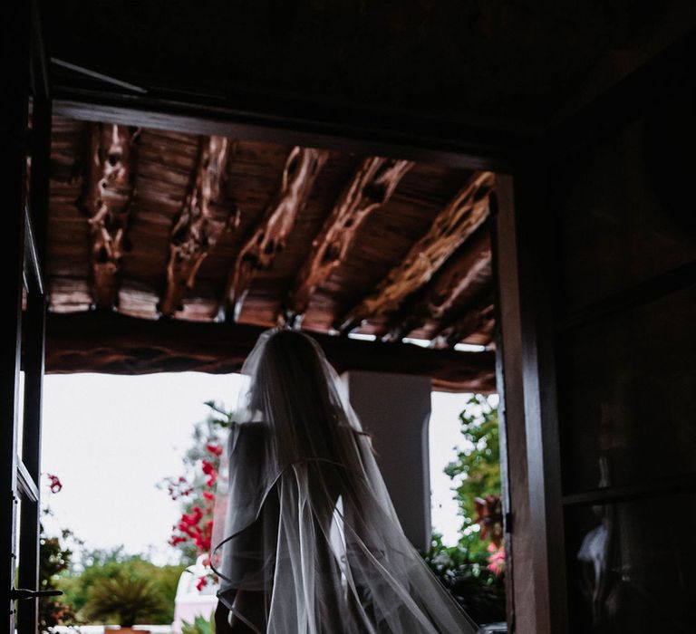 A bride walks out of her hotel room with long flowing veil. Photography by Stephanie Shenton.