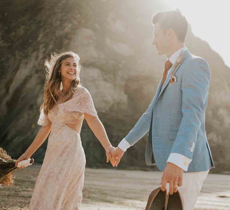 Bride and groom hold hands on beach in Cornwall