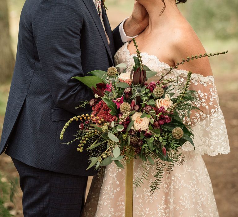 Bride & groom lean in to kiss whilst bride holds floral bouquet