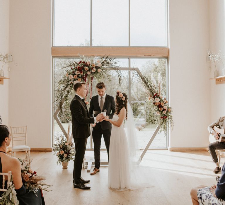 Boho ASOS wedding dress bride and groom in tuxedo exchanging vows in front of a hexagon wooden altar 