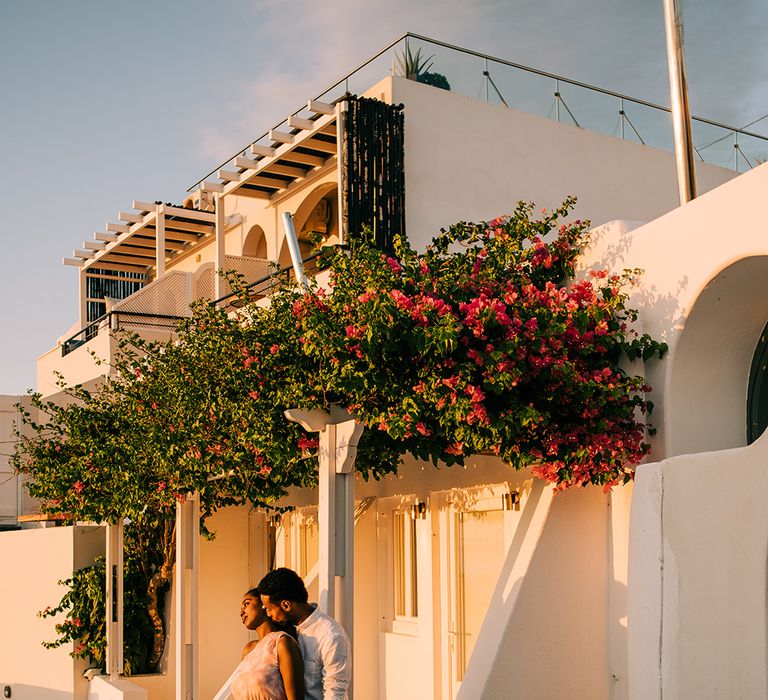 Groom kisses brides neck as they stand beside white houses in Santorini 