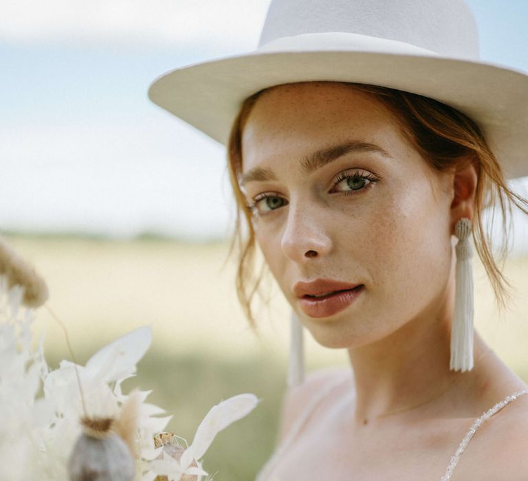 Bridal stetson hat, natural makeup, tassel earrings and an all white bouquet for boho wedding shoot at Berwick Lodge