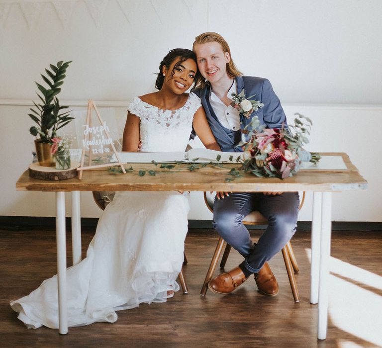 Bride and groom signing the register with a perspex sign and potted plant wedding decor on the table