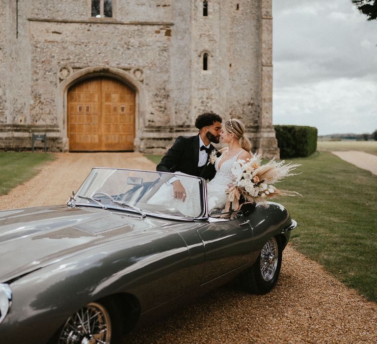 Bride and groom sitting in a classic convertible wedding car on the drive of Pentney Abbey