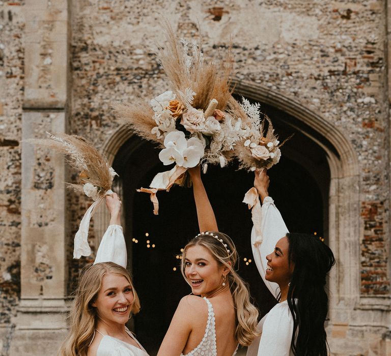 Bridal party portrait with bride and bridesmaids holding their neutral dried and fresh flower bouquets in the air 