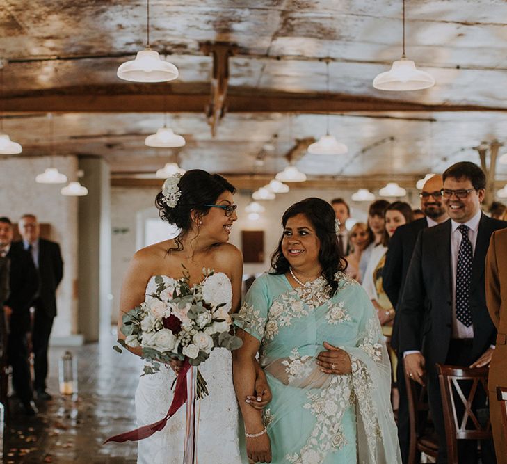 A Bangladeshi bride is walked down the aisle by her mum. she wears a Sophia Tolli gown and her Mom wears a light sea foam green traditional dress.