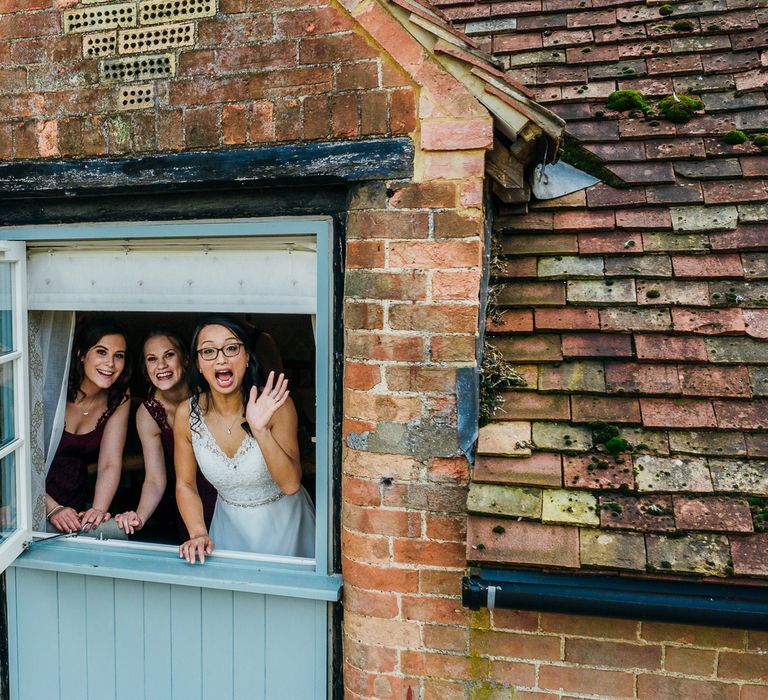 Bride smiles through window with bridal party on wedding day