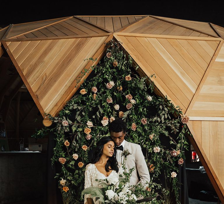 A couple stand in front of a flower arch for wedding portraits.