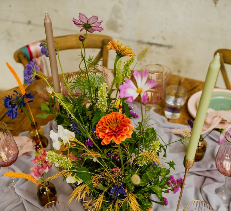 Fiesta theme wedding table decor with colourful wildflower centrepiece, taper candles, linens and coloured glassware 