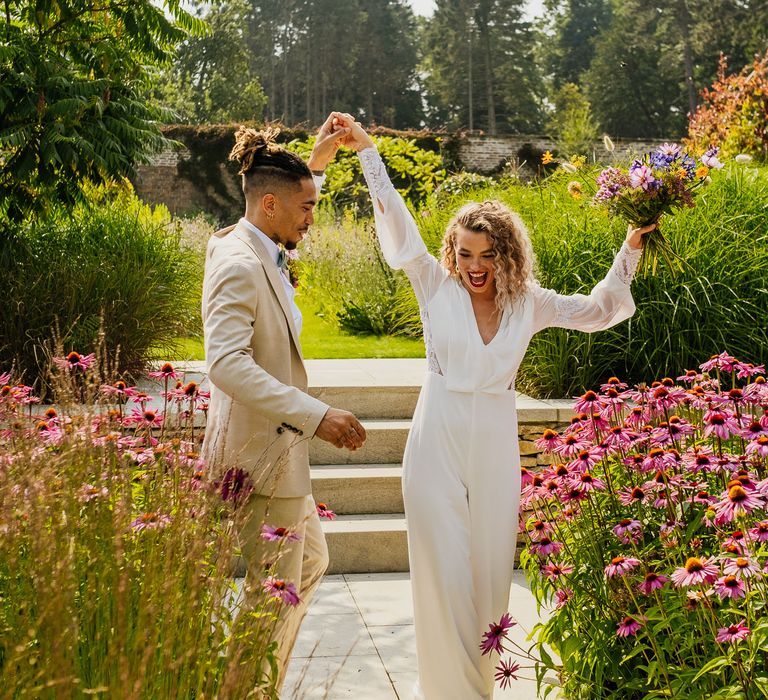 Groom in a beige suit twirling his bride in a jumpsuit in the Walled Gardens at The Fig House, Middleton Lodge 