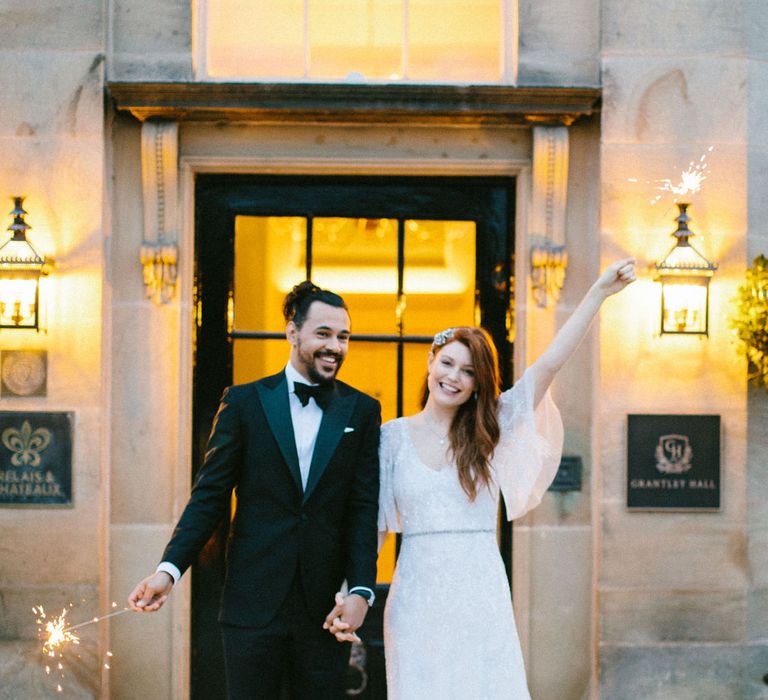 Sparkler moment outside Grantley Hall wedding venue with bride in a cap sleeve Eliza Jane Howell Paloma dress and groom in a tuxedo 