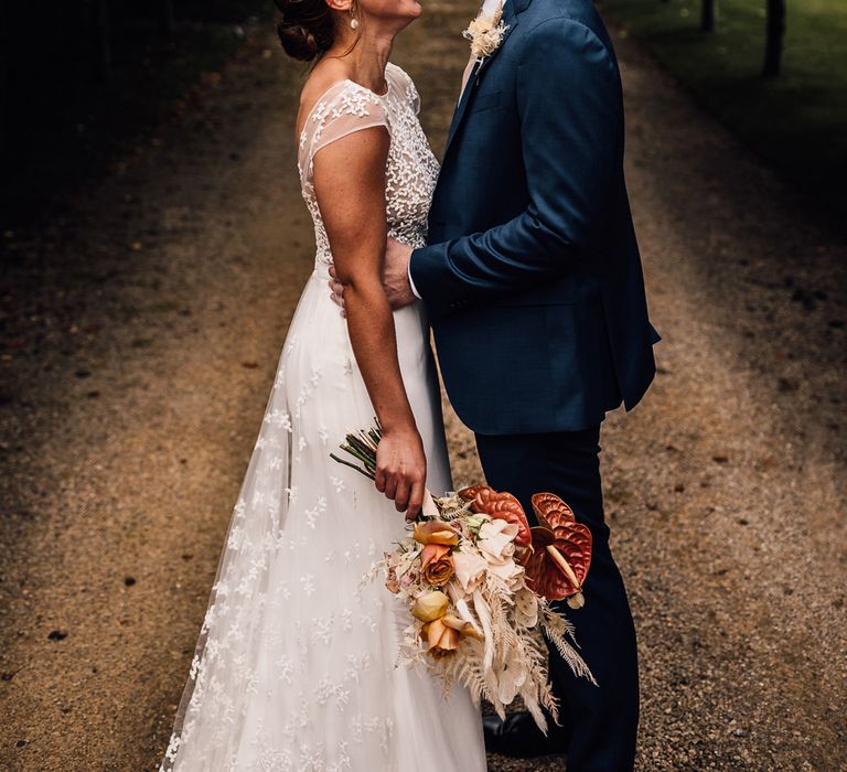 Bride in white Rime Arodaky wedding dress holding dried bridal bouquet smiles at groom in blue three piece suit outside after summer wedding in Dorset