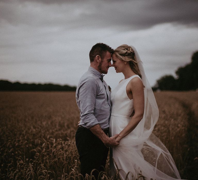 Bride & groom touch their foreheads against one another's outdoors as the brides dress and veil blows in the wind