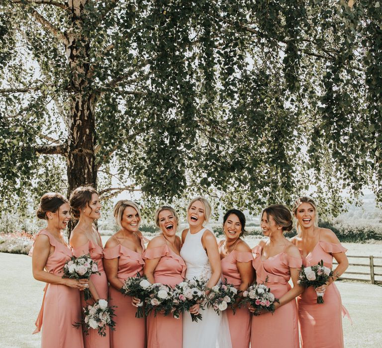 Bridal party portrait under a tree with bridesmaids in pink cold shoulder satin dresses with frills 