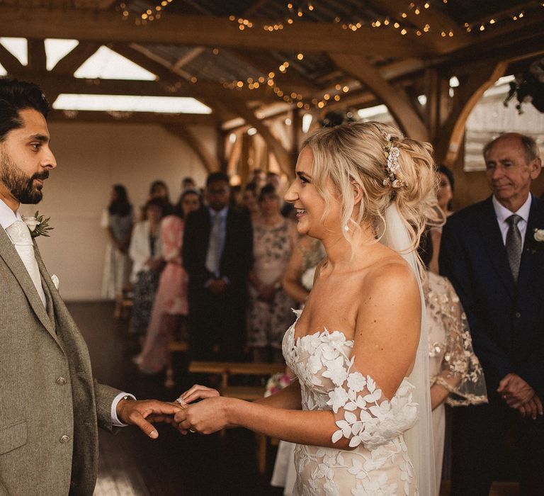 Bride in off the shoulder Enzoani wedding dress and veil holds hands with groom in grey suit with floral buttonhole during Inkersall Grange Farm wedding ceremony