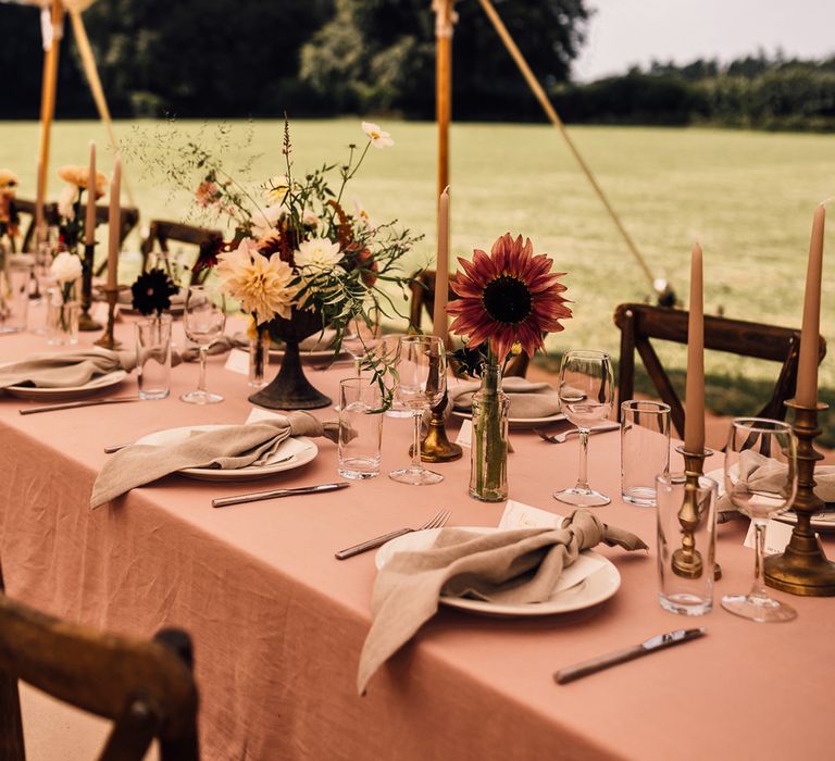 Two long wooden tables with dusky pink tablecloths, candles and assorted florals for marquee garden wedding reception in Cornwall