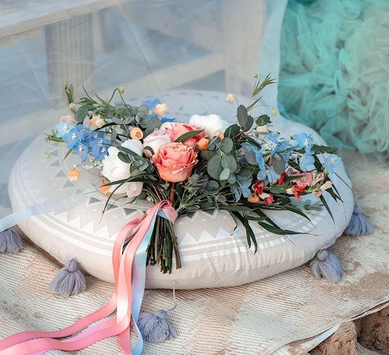 Pastel wedding bouquet with coral roses, eucalyptus foliage and white peonies tied with ribbon 