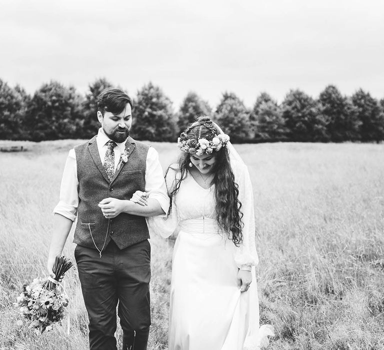 Bride & groom walk arm in arm with one another in field on their wedding day