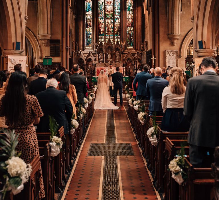 Interior or church with bride in white dress with train and groom in blue checked suit standing at the altar during church wedding ceremony