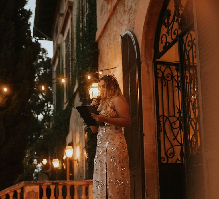 Bride gives speech on balcony on her wedding day as candles are lined around her