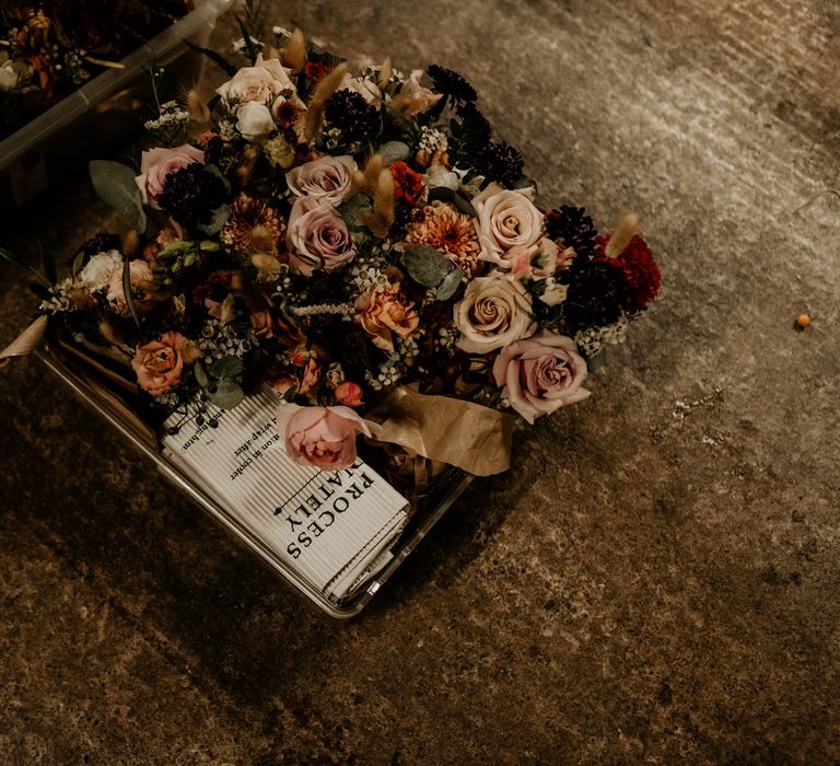 Mixed dusty wedding florals with pink roses and foliage in basket for rustic wedding