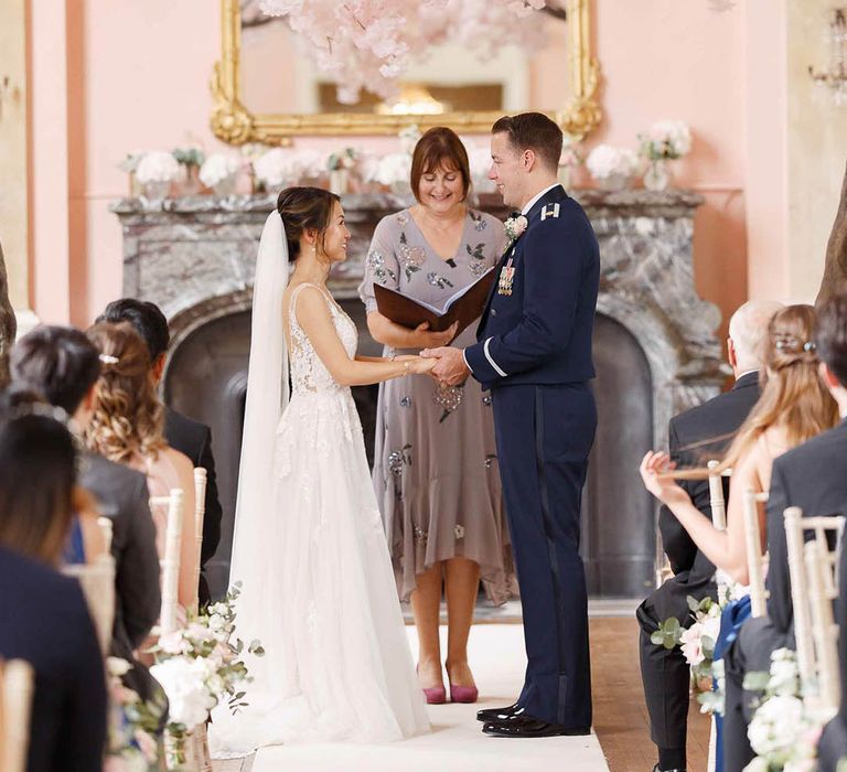 Bride & groom hold hands during wedding ceremony as celebrant reads 