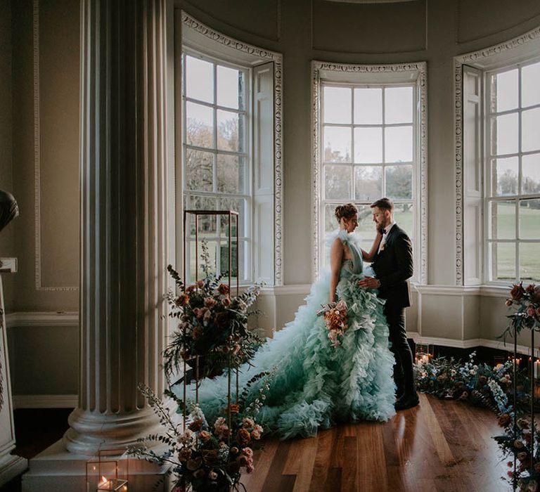 Bride in a light blue wedding dress holding a pink and cafe au late wedding bouquet with her groom in a tuxedo at Newburgh Priory