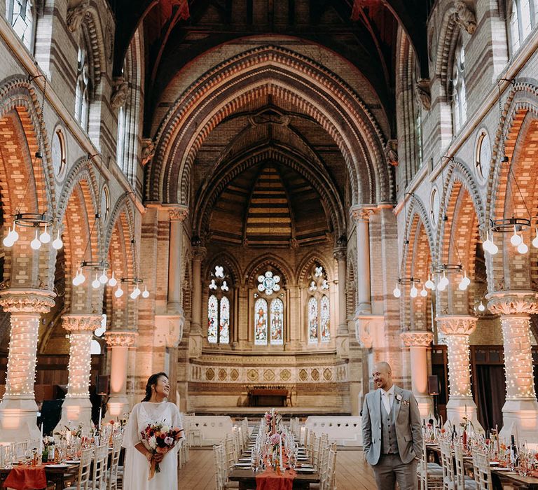 Bride & groom look across to one another on their wedding day between wooden tables 