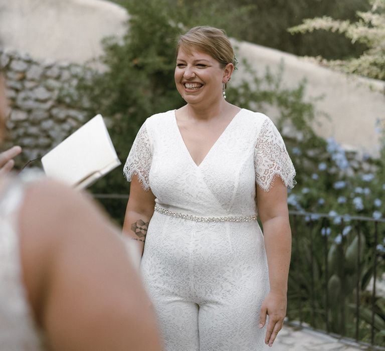 Bride in lace wedding jumpsuit and diamanté belt at the altar