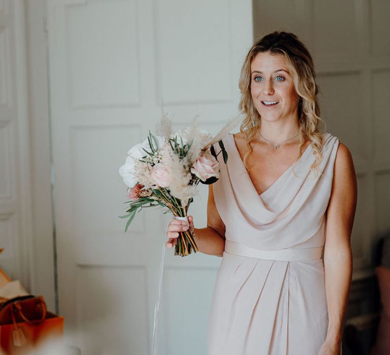 First look with bridesmaid in a pink cowl neck bridesmaid dress holding a rose bouquet 