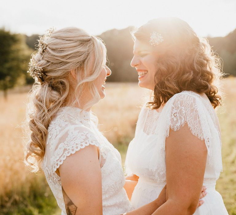 Brides laugh together at golden hour in white wedding dresses with sheer high neck design