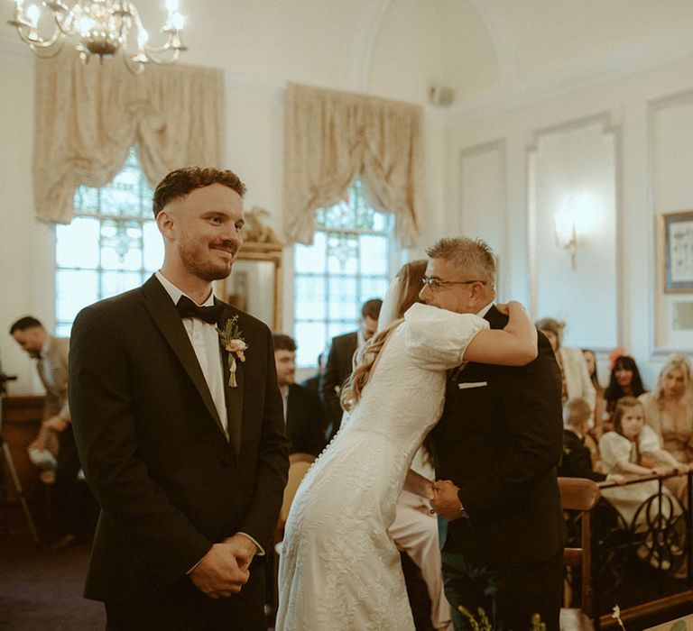 Bride hugs her father in black tie as she gets ready to marry her groom also in black tie for registry office wedding