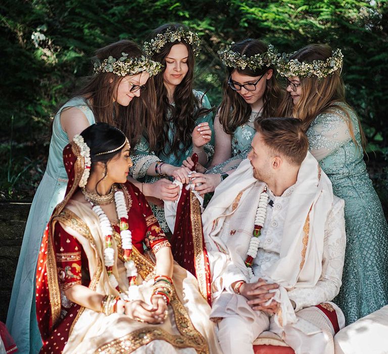 Bride and groom are seated at multicultural wedding with bridesmaids in sage green dresses and matching flower crowns