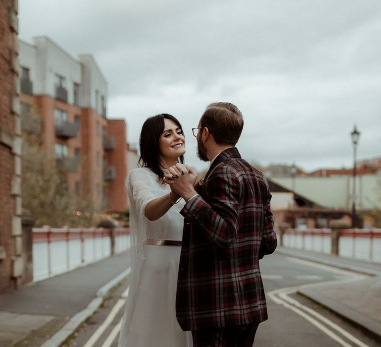 Bride looks lovingly at her groom outdoors on her wedding day as she wears lace cape 