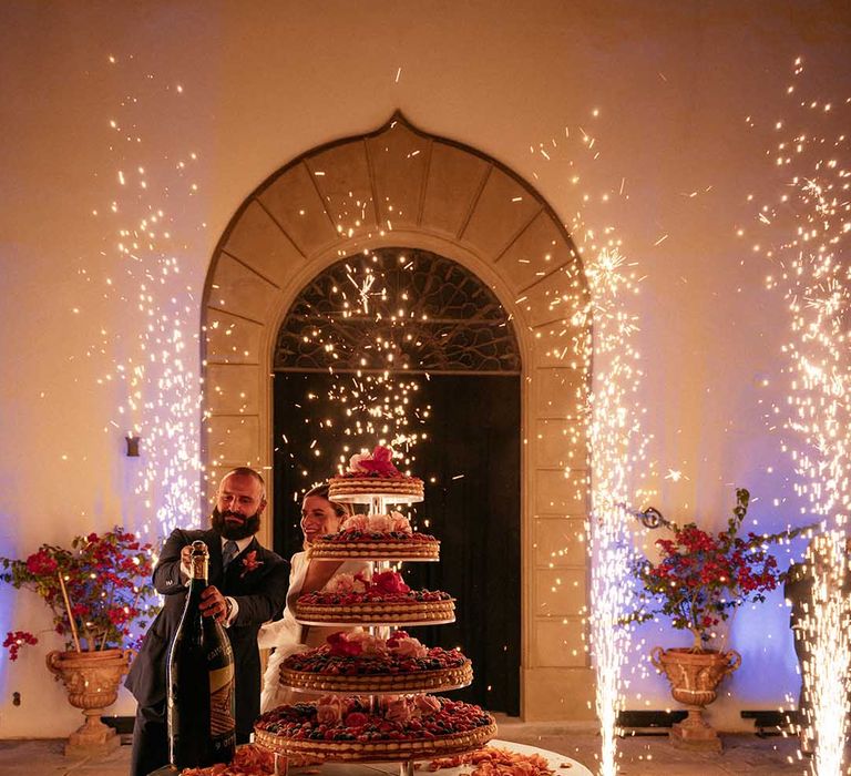 Bride & groom pop champagne on their wedding day surrounded by sparklers 