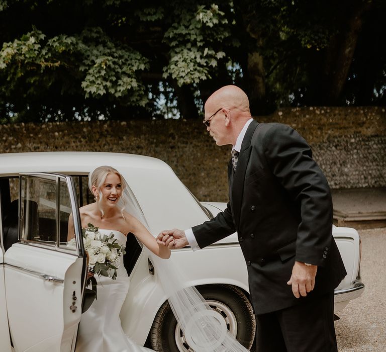 Guest helps the bride in a strapless gown out of her white wedding car transportation 